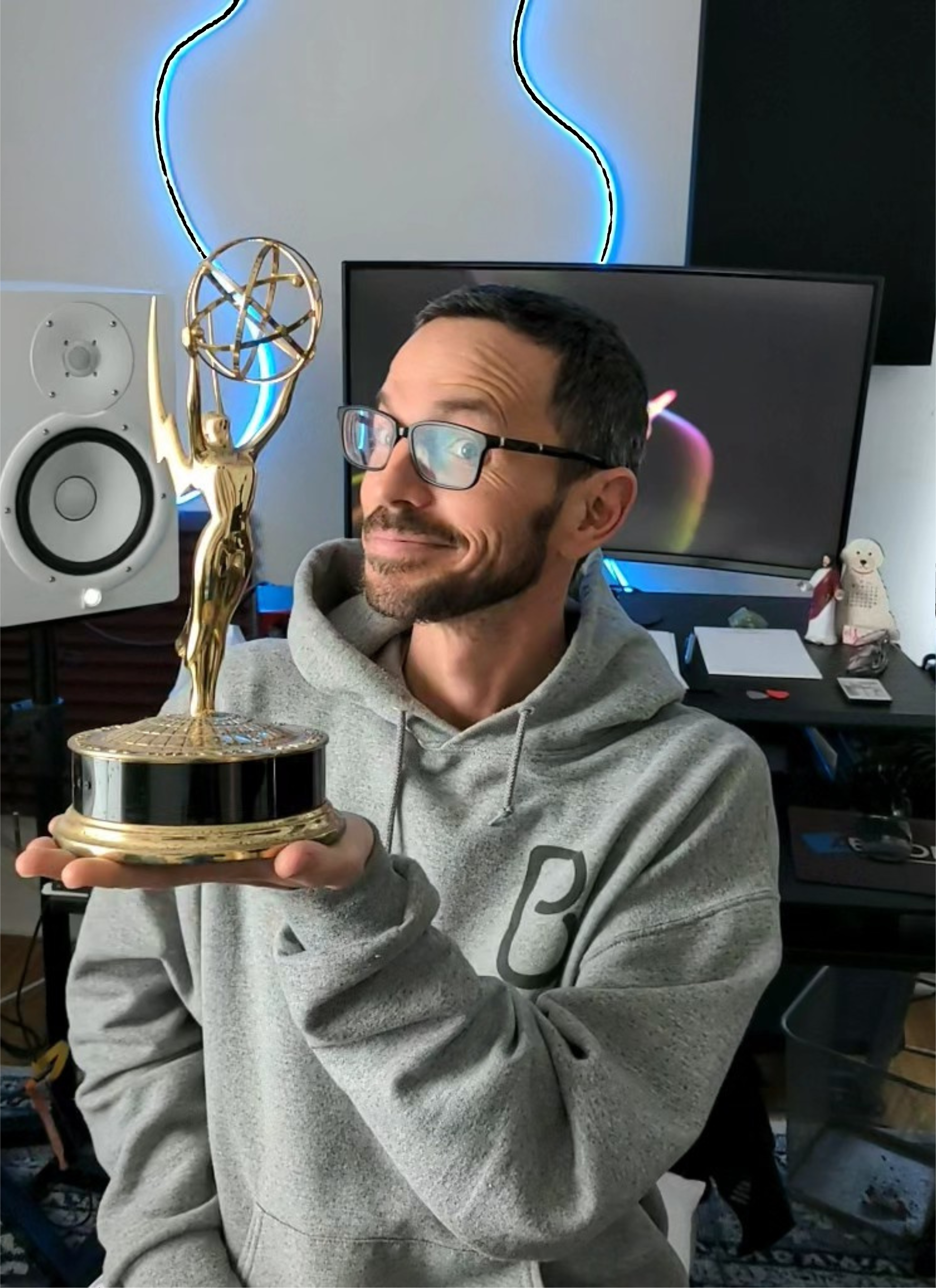 A picture of a man with black hair wearing glasses and a grey sweatshirt holding a trophy.