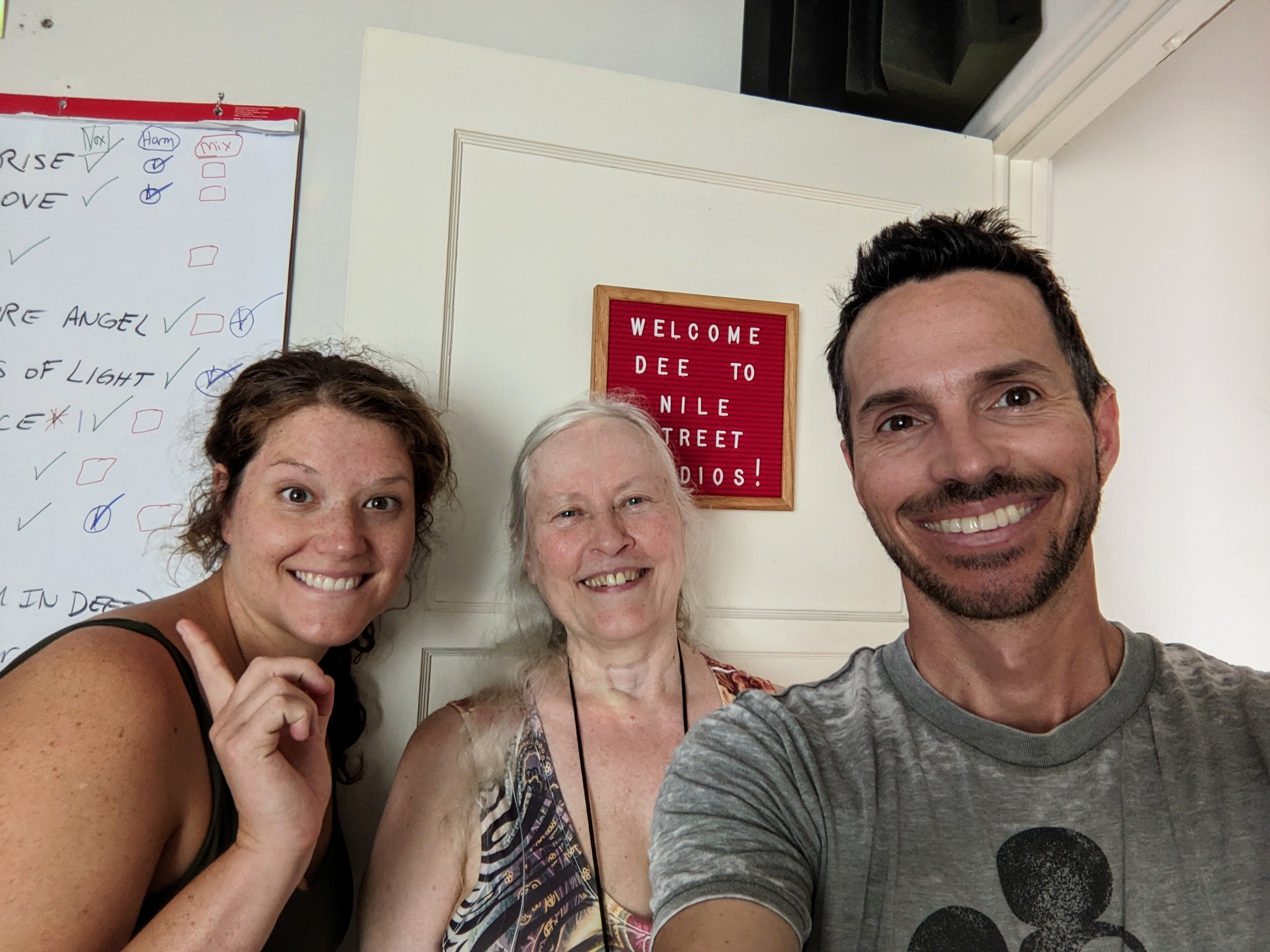 A picture of Laura Rose, Deloris Wirak, TJ Moss standing in front of a red sign reading 'WELCOME DEE TO NILE STREET STUDIO!'
